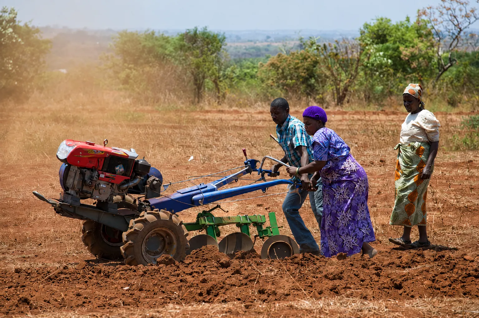 Farmers working a field with a two-wheel tractor and disc implement